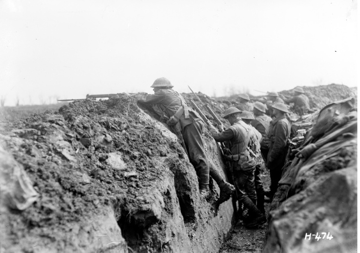 New Zealand soldiers in a front-line trench on the Somme, La Signy Farm, France, 6 April 1918. Sergeant Ormond Burton (Auckland Regiment's official historian who became a prominent Second World War conscientious objector) stands on a firing step in the trench wall [photo Henry Armytage Sanders, Alexander Turnbull Library, ref no: 1/2-013092-G]